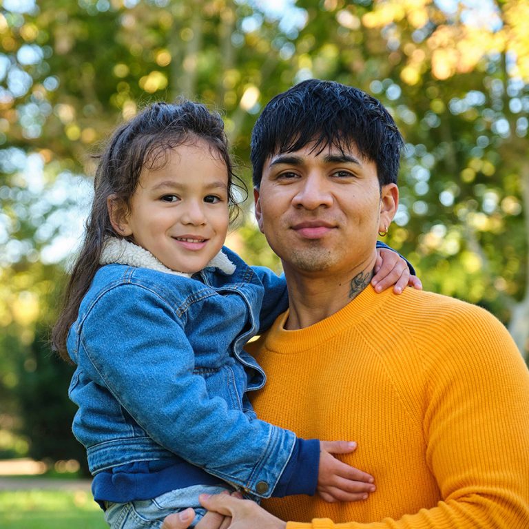 Portrait of happy Ecuadorian father holding his son in a park.